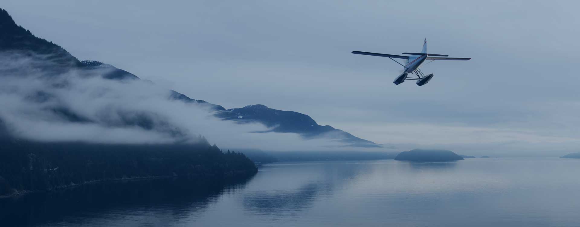 Floatplane flying low over misty water along a mountainous coast