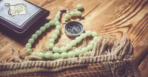 Prayer beads, prayer mat, compass, and book on a wood floor
