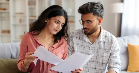 Couple sitting on a couch reviewing financial documents together at home