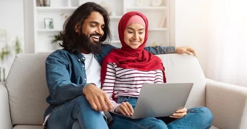 Couple sitting on a sofa and reviewing information together on a laptop at home